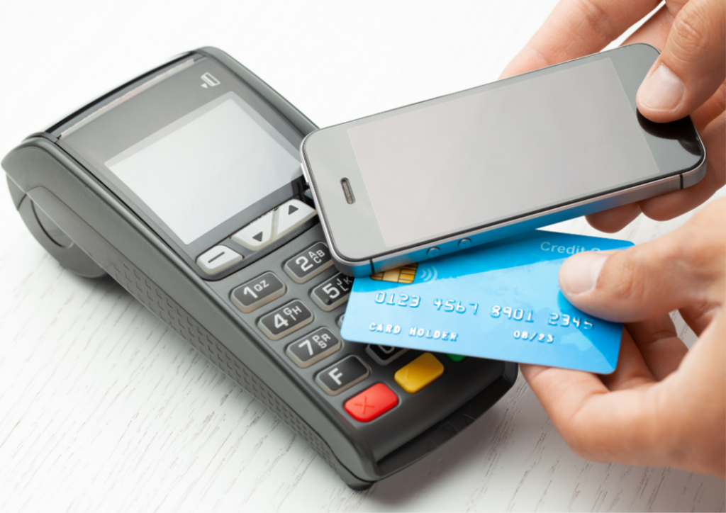 Image with a credit card reader and a person paying using a mobile phone via contactless payments.