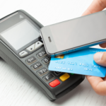 Image with a credit card reader and a person paying using a mobile phone via contactless payments.