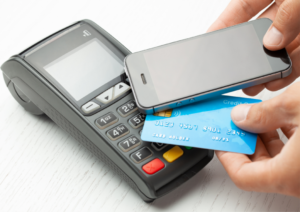 Image with a credit card reader and a person paying using a mobile phone via contactless payments.